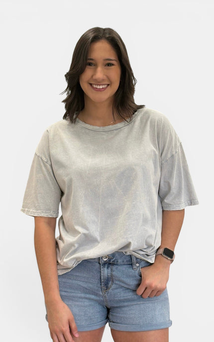 A woman wearing a light gray mineral-wash short-sleeve t-shirt and light blue denim shorts, standing against a plain white studio background.