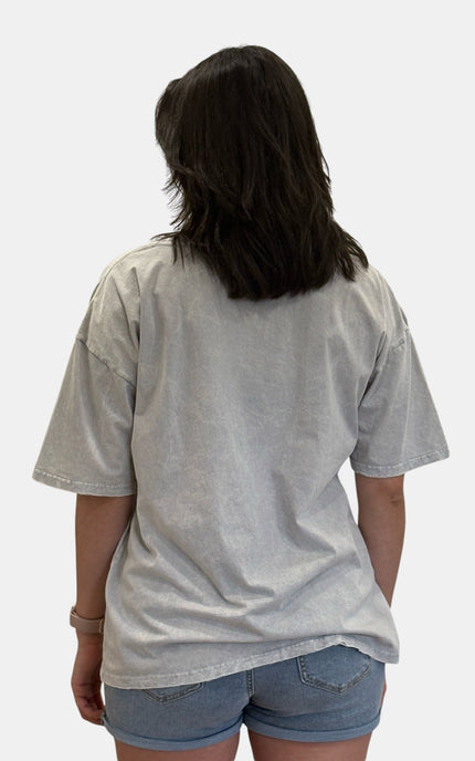A person shown from the back wearing an oversized light gray washed short-sleeve t-shirt and denim shorts against a plain light gray background.