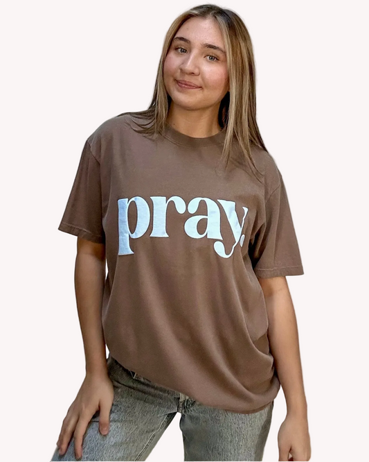 Person wearing a brown t-shirt with 'pray' printed on it against a plain background