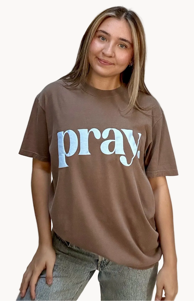 Person wearing a brown t-shirt with 'pray' printed on it against a plain background
