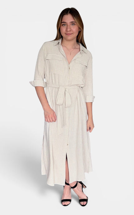 A woman modeling a cream and white vertically striped midi shirt dress with a tie waist belt, three-quarter sleeves, and a front slit, paired with black strappy heels against a light gray studio background.
