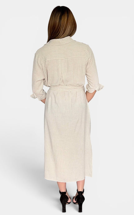 A woman viewed from the back wearing a cream-colored midi shirt dress with thin vertical stripes, ruffled three-quarter sleeves, and a matching tie belt. She is wearing black high-heeled sandals against a light gray studio background.
