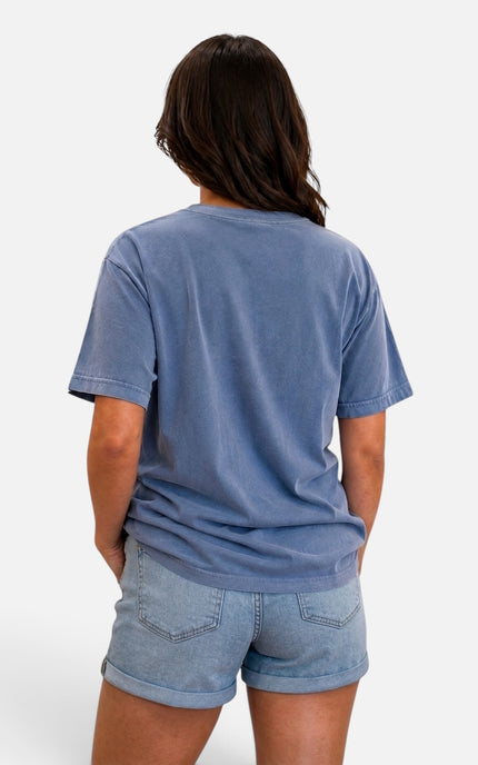 A woman shown from the back wearing a washed medium blue short-sleeve t-shirt and light blue denim shorts against a light gray studio background.