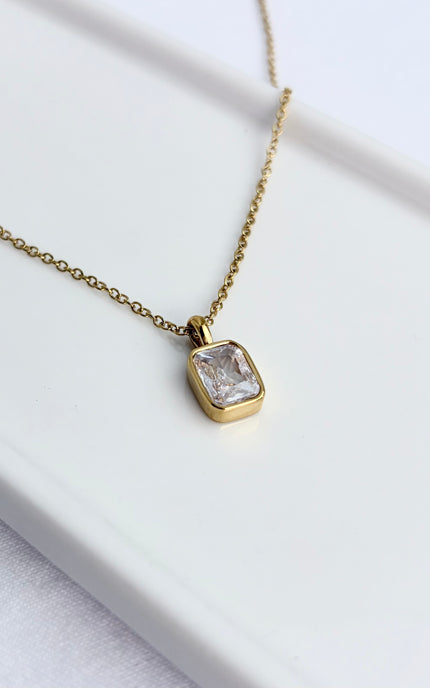 Gold necklace with a clear gemstone pendant on a white surface