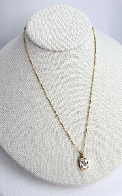 Gold rectangular zircon pendant necklace displayed on a neutral jewelry form, showing its clean, minimal silhouette.