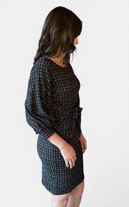 A woman wearing a black plaid dress, shown from a side profile against a plain light gray background.