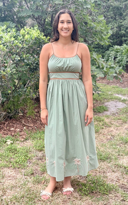 Woman in a green dress standing outdoors with greenery in the background