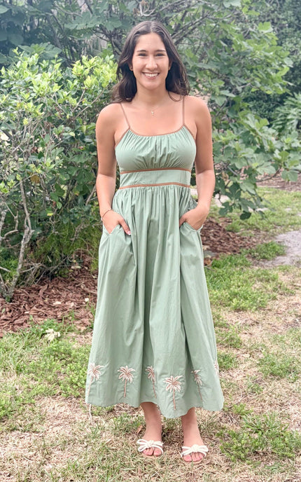 Woman wearing a green dress with floral embroidery standing outdoors.