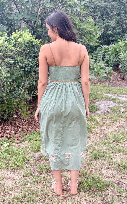 Woman wearing a green dress with floral embroidery standing outdoors.