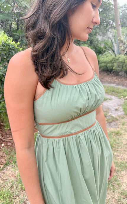 Woman wearing a light green dress standing outdoors with greenery in the background