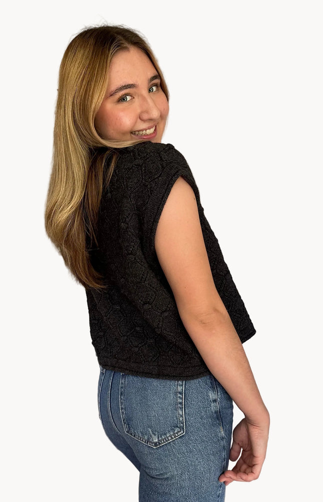 Woman wearing a black sleeveless top and blue jeans in a kitchen.