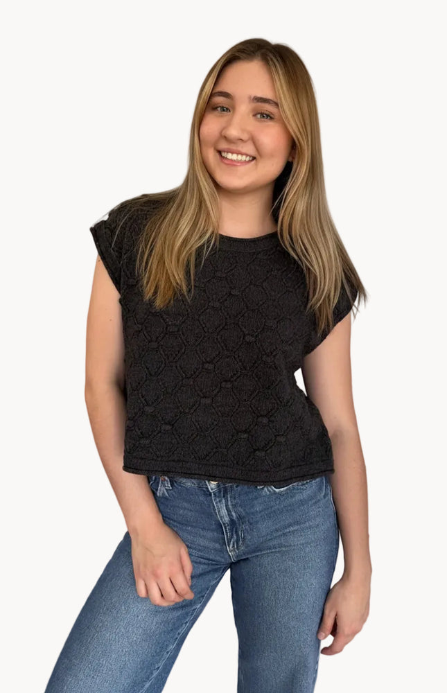 Young woman wearing a black lace top and blue jeans on a plain background