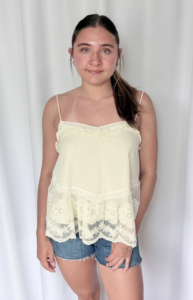 Front view of a soft, white 100% cotton camisole featuring a V-neckline with delicate lace trim, mini ruffles, and a central embroidered floral mesh panel with scalloped edges.