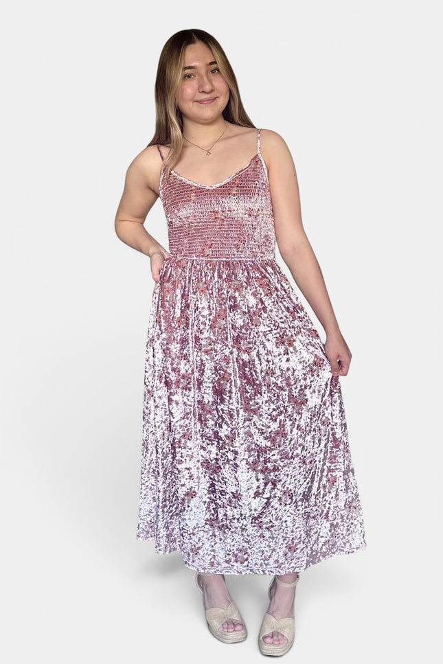 Sleeveless midi dress with thin straps, featuring a smocked bodice and a crinkled, textured skirt in a dusty rose and white pattern, set against a plain light gray background.
