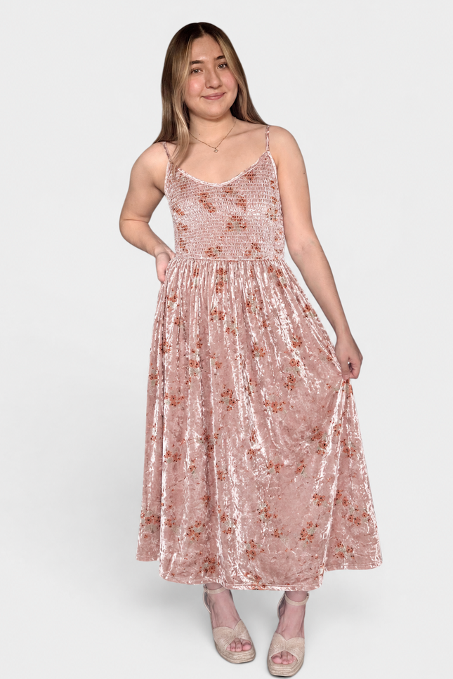 A woman modeling a sleeveless, midi-length pink velvet dress with a subtle floral pattern, photographed against a solid light gray background.
