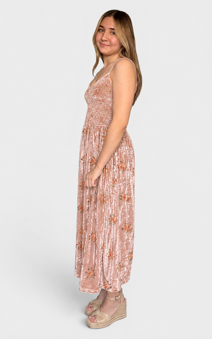 A woman modeling a sleeveless, floor-length dusty rose maxi dress with a subtle floral pattern and velvet fabric, paired with beige wedge sandals, against a light gray studio background.