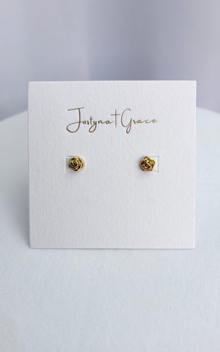 A pair of delicate 18k gold PVD rose stud earrings sitting securely on a soft jewelry card, emphasizing their classic, high-quality finish.
