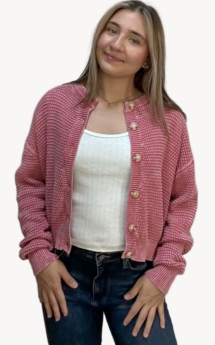 Woman wearing a pink cardigan over a white top and blue jeans on a plain background