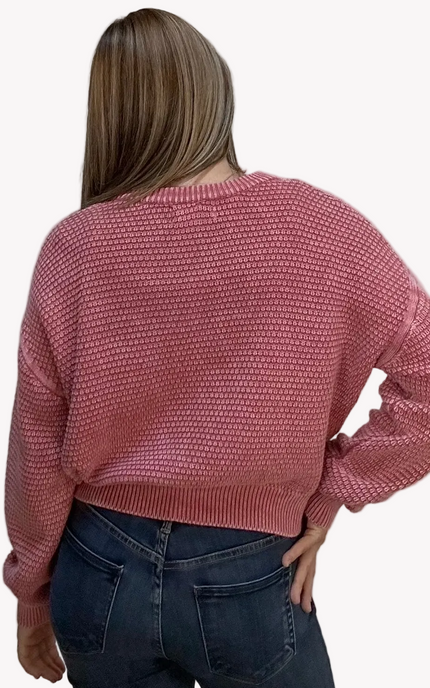 Person wearing a pink textured sweater and blue jeans on a light gray background