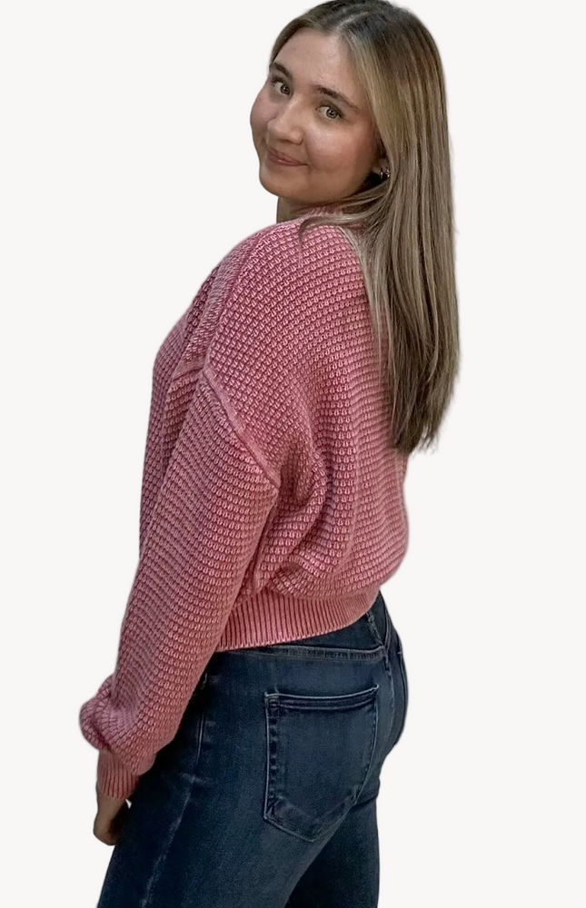 Woman wearing a pink sweater and dark jeans on a light pink background