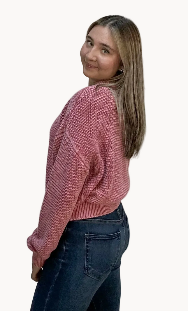 Woman wearing a pink sweater and dark jeans on a light pink background