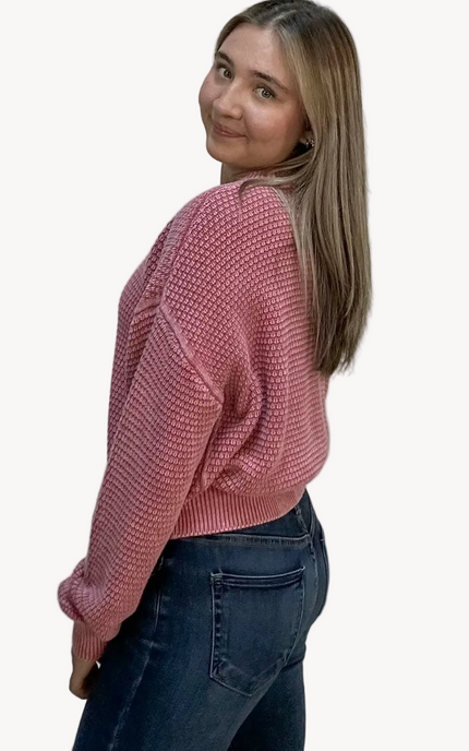 Woman wearing a pink sweater and dark jeans on a light pink background