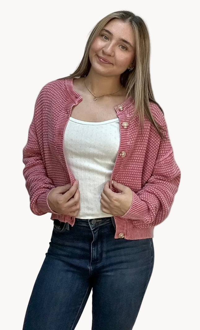 Woman wearing a pink knitted cardigan over a white top and dark jeans on a light pink background