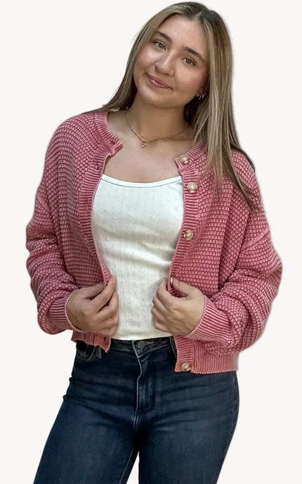 Woman wearing a pink knitted cardigan over a white top and dark jeans on a light pink background
