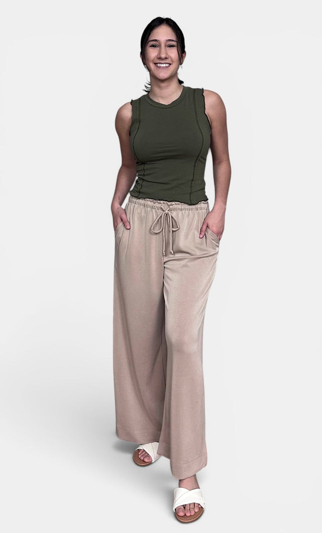 A woman modeling a sleeveless olive green top and wide-leg beige drawstring pants against a light gray studio background.