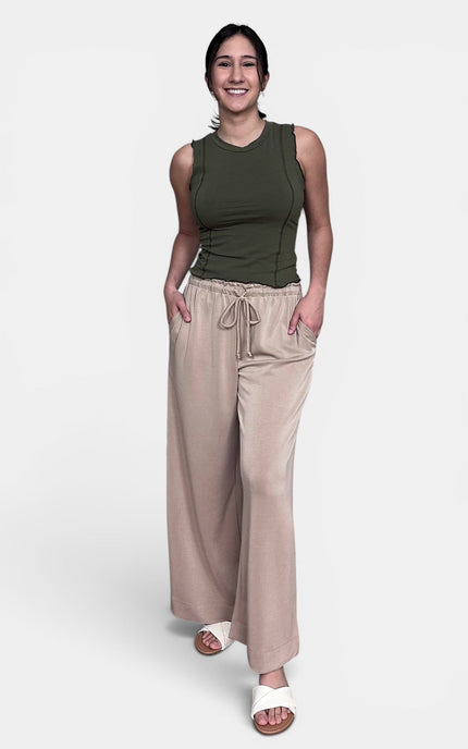 A woman modeling a sleeveless olive green top and wide-leg beige drawstring pants against a light gray studio background.