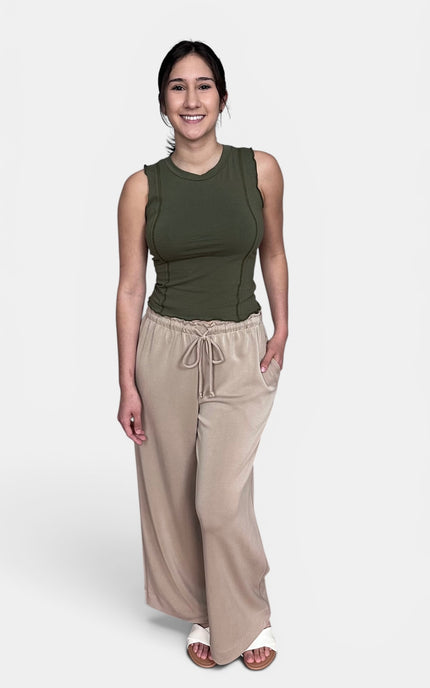 A woman modeling a sleeveless olive green top and beige wide-leg drawstring pants against a light gray studio background.