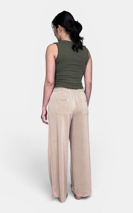 A woman shown from the back wearing a sleeveless olive green top and light beige wide-leg trousers against a plain light gray studio background.