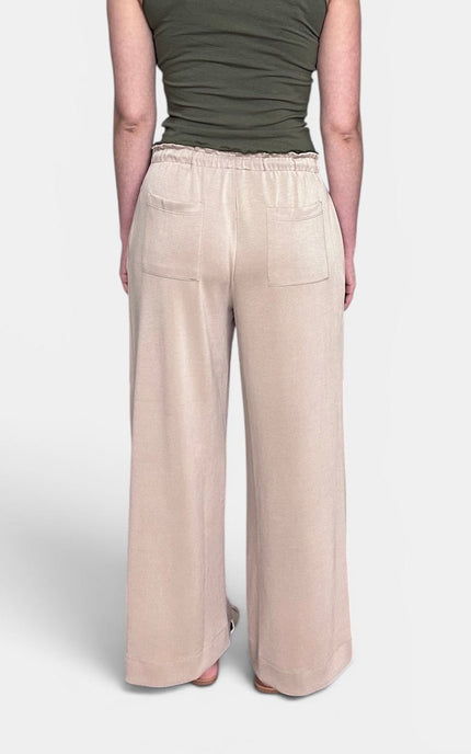 A person shown from the back wearing wide-leg beige pants with an elastic waistband and two back patch pockets, paired with an olive green sleeveless top, against a light gray studio background.