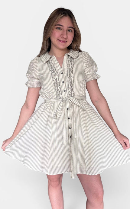 A young woman modeling a short-sleeve cream and white vertically striped dress with a ruffled collar, button front, and tie waist, set against a plain light gray studio background.