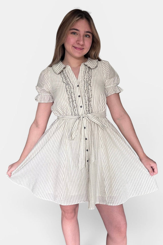 A young woman modeling a short-sleeve cream and white vertically striped dress with a ruffled collar, button front, and tie waist, set against a plain light gray studio background.