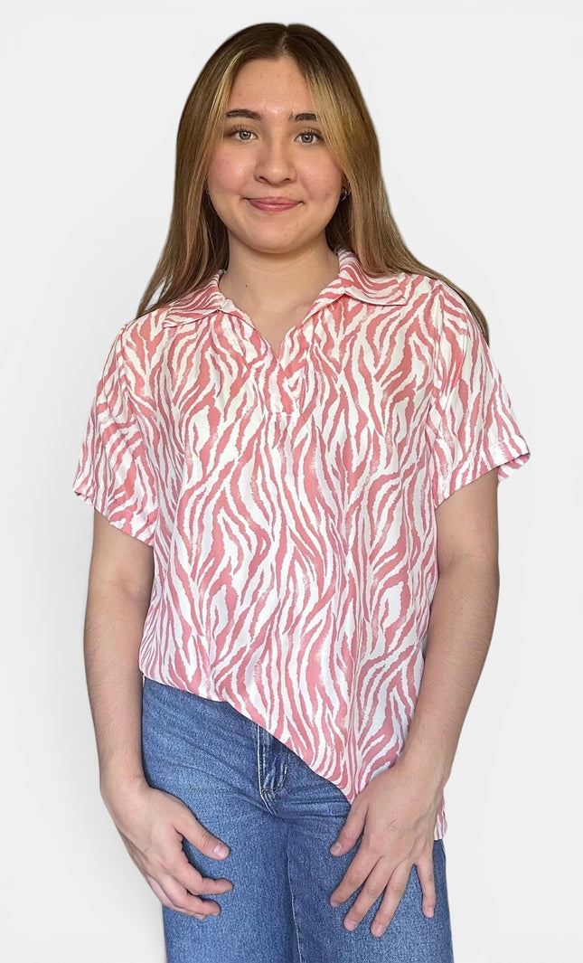 Short-sleeve collared button-up shirt with a pink and white zebra-like abstract pattern, paired with blue jeans, against a plain light gray background.