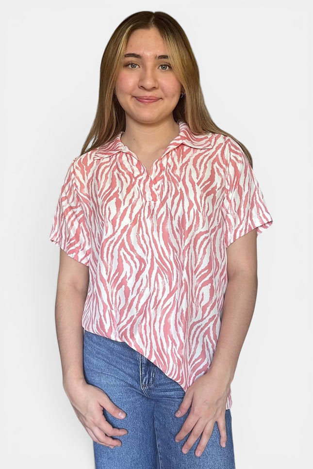 Short-sleeve collared button-up shirt with a pink and white zebra-like abstract pattern, paired with blue jeans, against a plain light gray background.