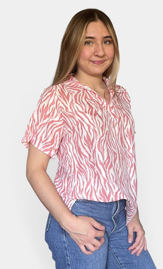 Short-sleeve button-up blouse with a pink and white zebra-like abstract pattern, paired with blue jeans, against a light gray background.