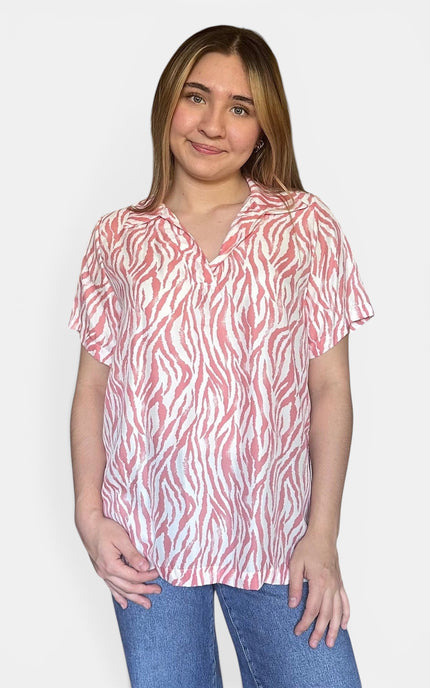 Short-sleeve collared blouse with a pink and white zebra-like abstract print, paired with blue jeans, against a plain light gray background.
