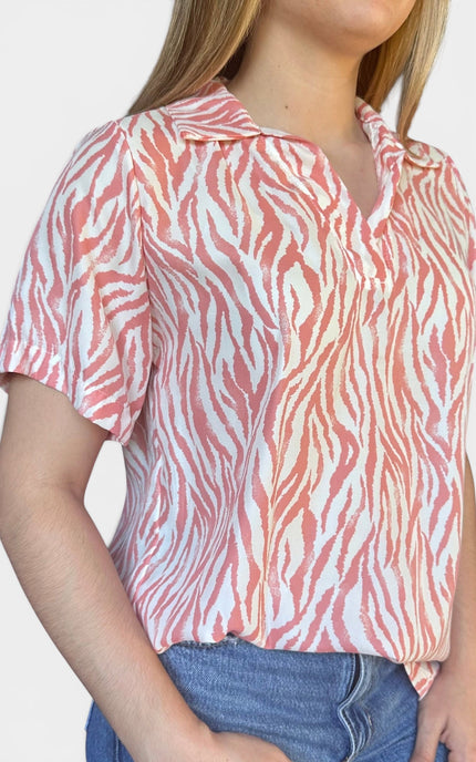 Short-sleeve collared blouse with a pink and white zebra-like stripe pattern, paired with blue jeans, shown against a plain light background.