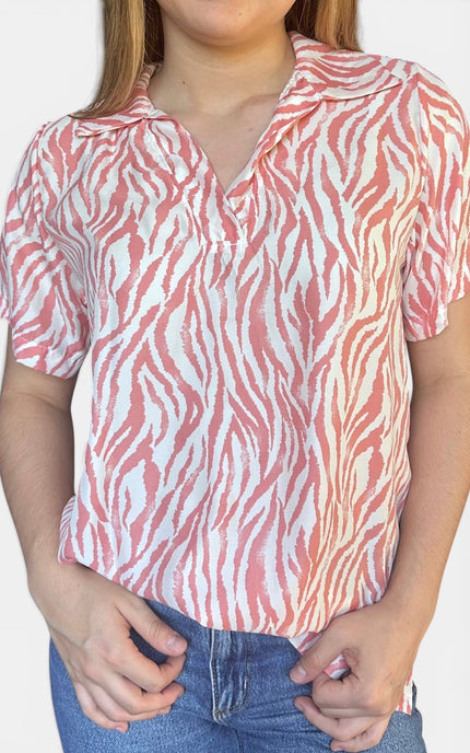 Short-sleeve collared blouse with a coral pink and white zebra-like abstract pattern, paired with blue jeans against a plain light background.