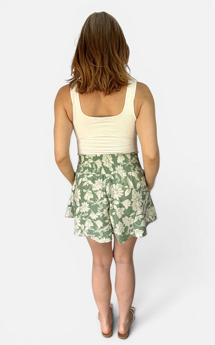 A woman shown from the back wearing a cream ribbed tank top and a green and cream floral tiered skirt, photographed against a light gray studio background.
