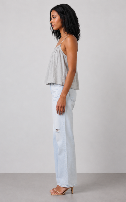 Woman wearing a light gray sage top and light blue jeans against a white background