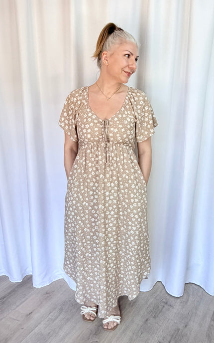 Woman wearing a floral dress standing against a white curtain