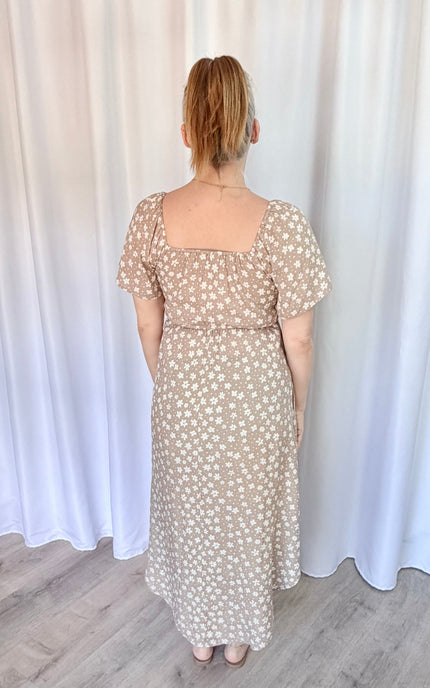 Woman wearing a floral dress standing against a white curtain.