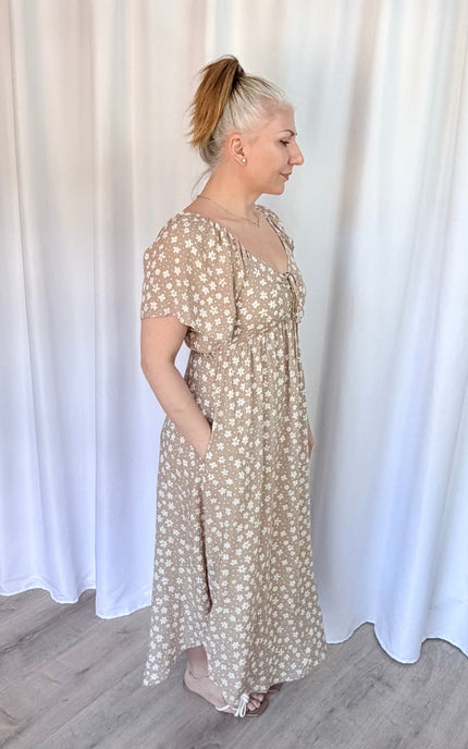 Woman wearing a beige floral dress against a white curtain background