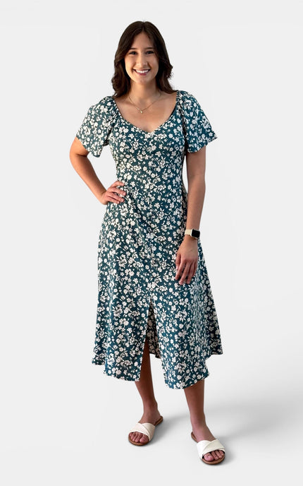 Woman wearing a teal floral midi dress with a princess neckline, button front, and flared sleeves.