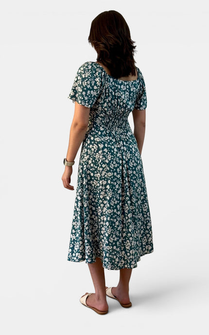 Back angled view of a teal floral midi dress with flared sleeves and a flowing midi-length skirt.