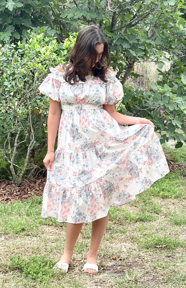 Model wearing a romantic floral off-shoulder midi dress with tiered skirt and puff sleeves, styled for a summer celebration