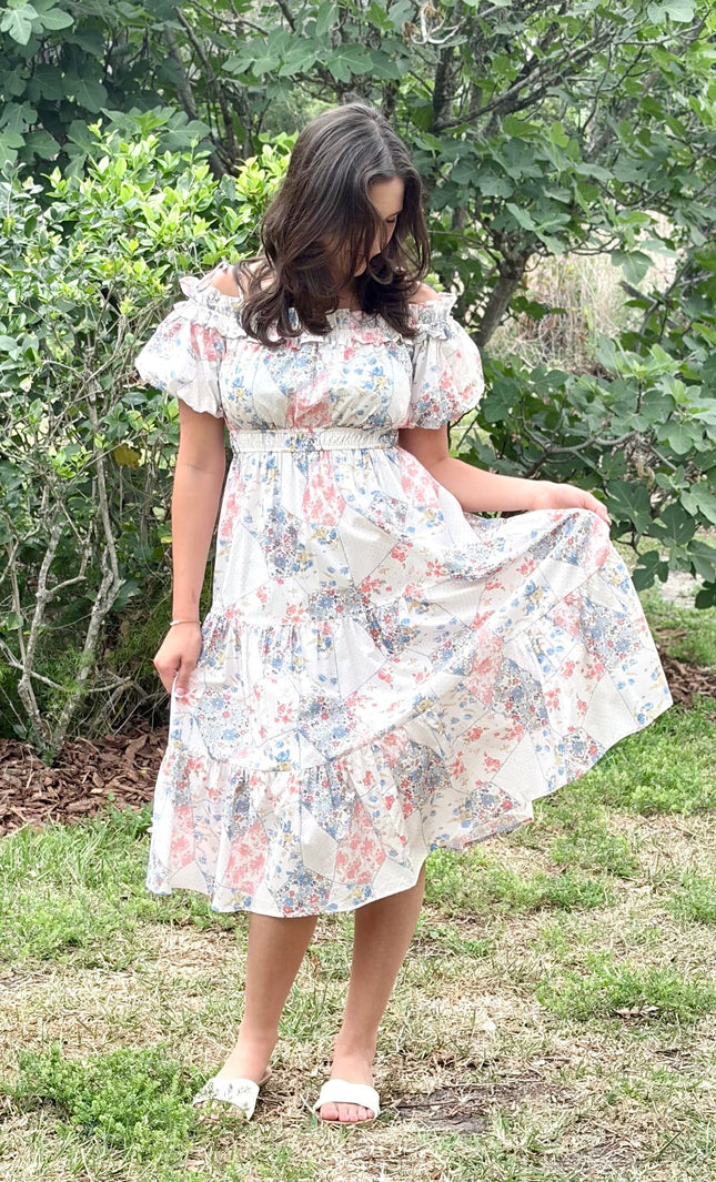 Model wearing a romantic floral off-shoulder midi dress with tiered skirt and puff sleeves, styled for a summer celebration